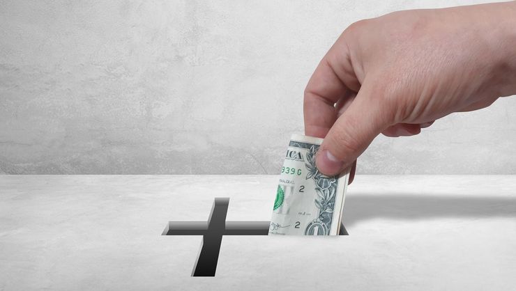 A hand is putting a dollar bill into a box with a cross on it.