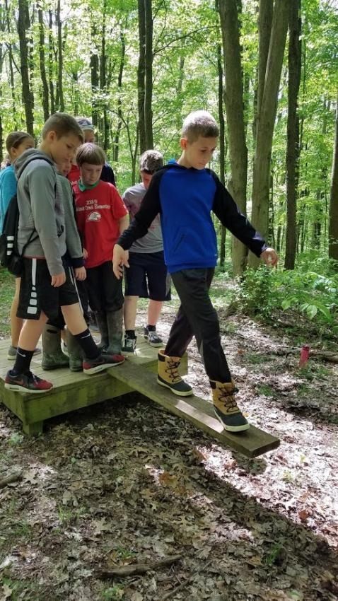A group of young boys are walking across a wooden bridge in the woods.