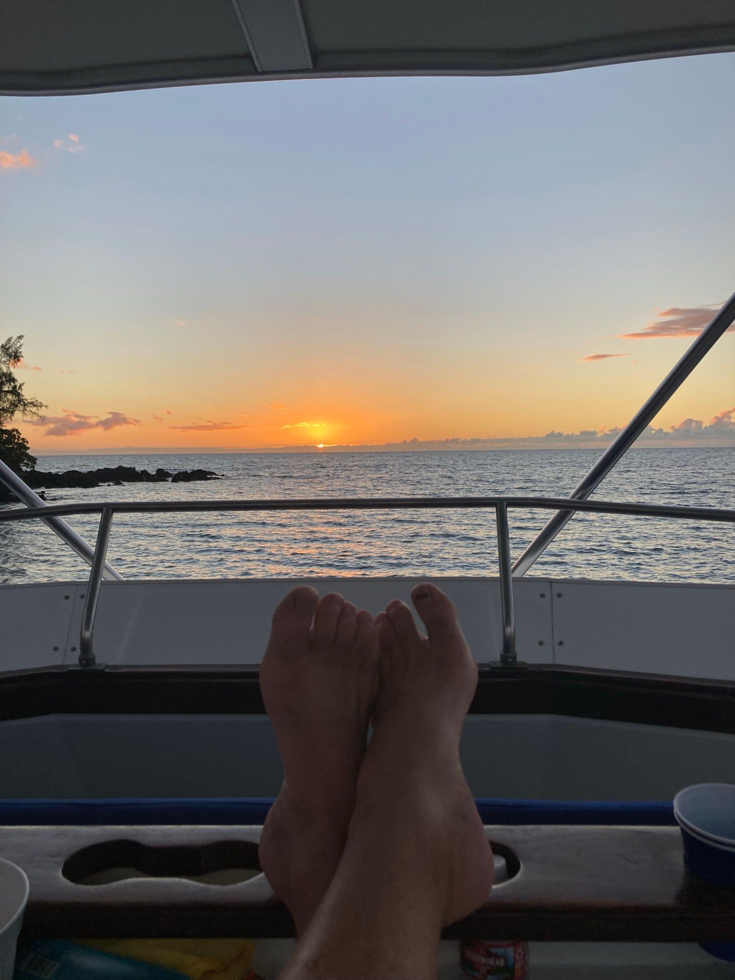 A person is sitting on a boat with their feet up watching the sunset over the ocean.