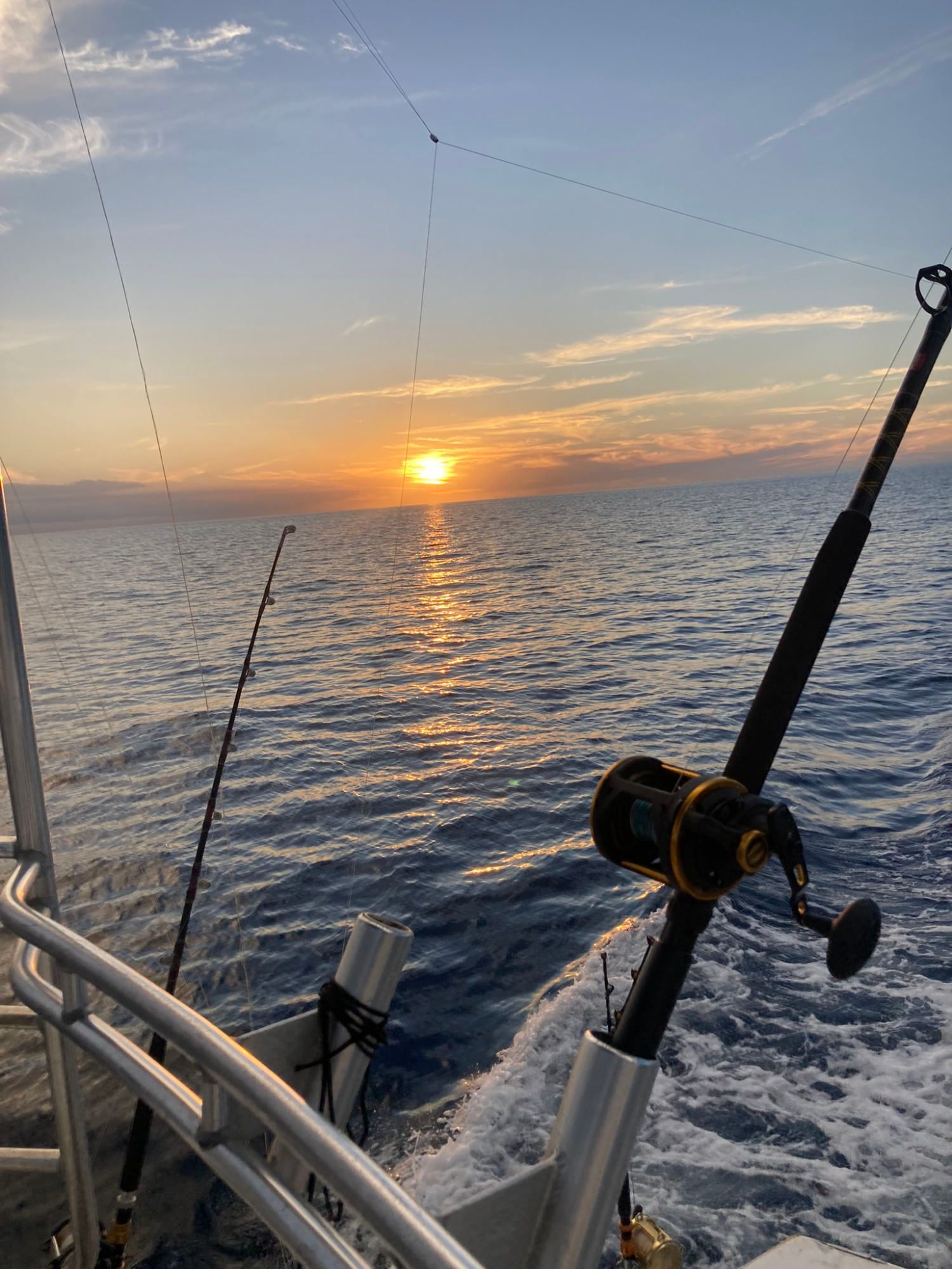 A fishing rod is sitting on a boat in the ocean at sunset.