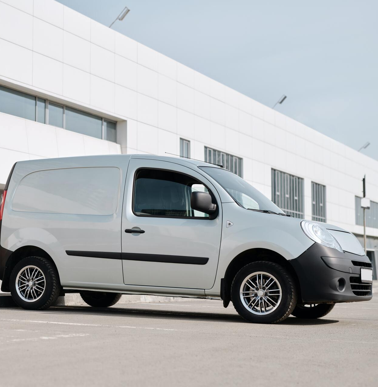 Een witte bestelwagen staat geparkeerd voor een gebouw