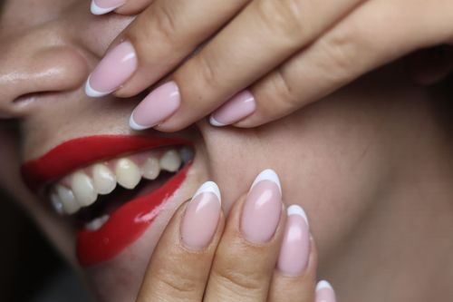 Person smiling, showing teeth, red lipstick. French manicure, pale pink nails with white tips.