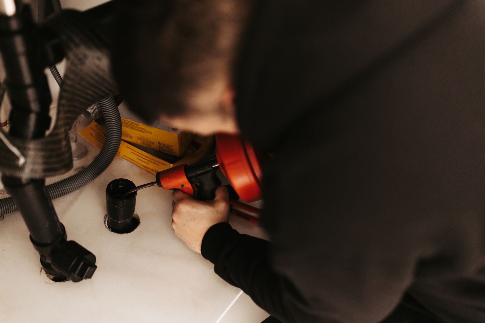 Person using a red and black plumbing snake to unclog a drain.