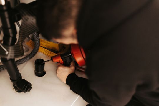 Person using a drain snake tool under a sink.