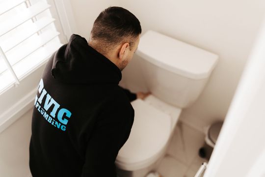 A person in a black hoodie checks a toilet in a bathroom.