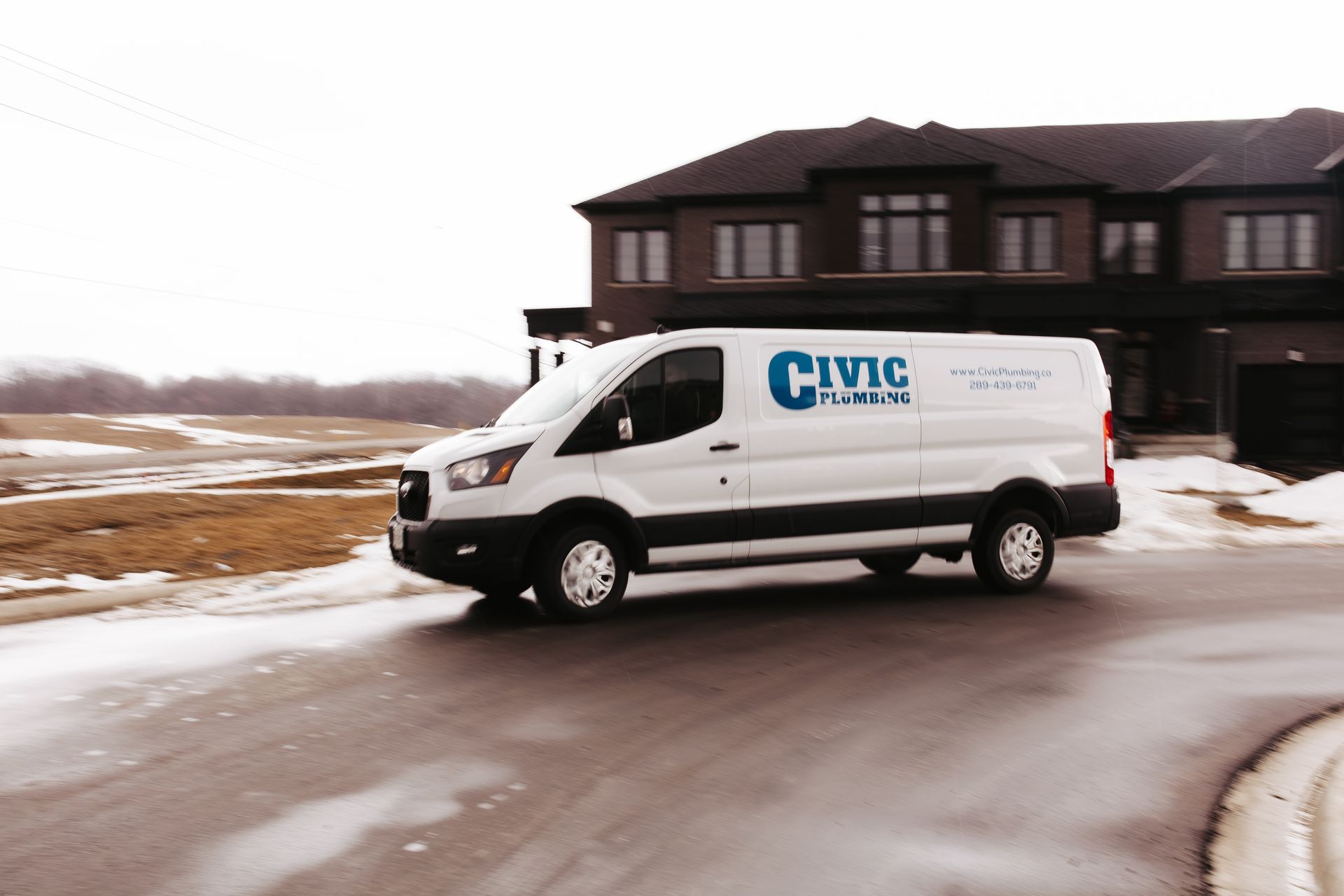 White Civic Plumbing van parked on a wet road in front of a house. Winter scene.
