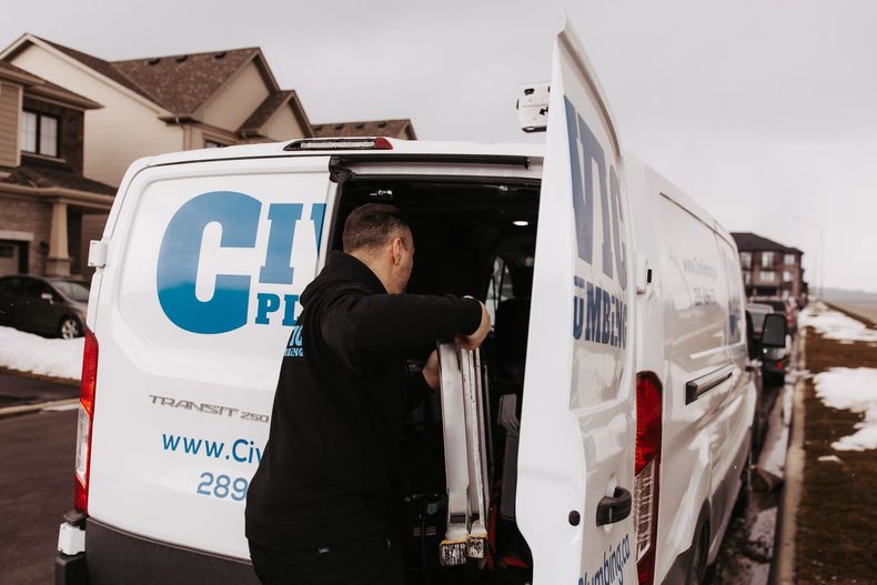 A technician in black loading equipment from a white van with blue logo. Houses in background.