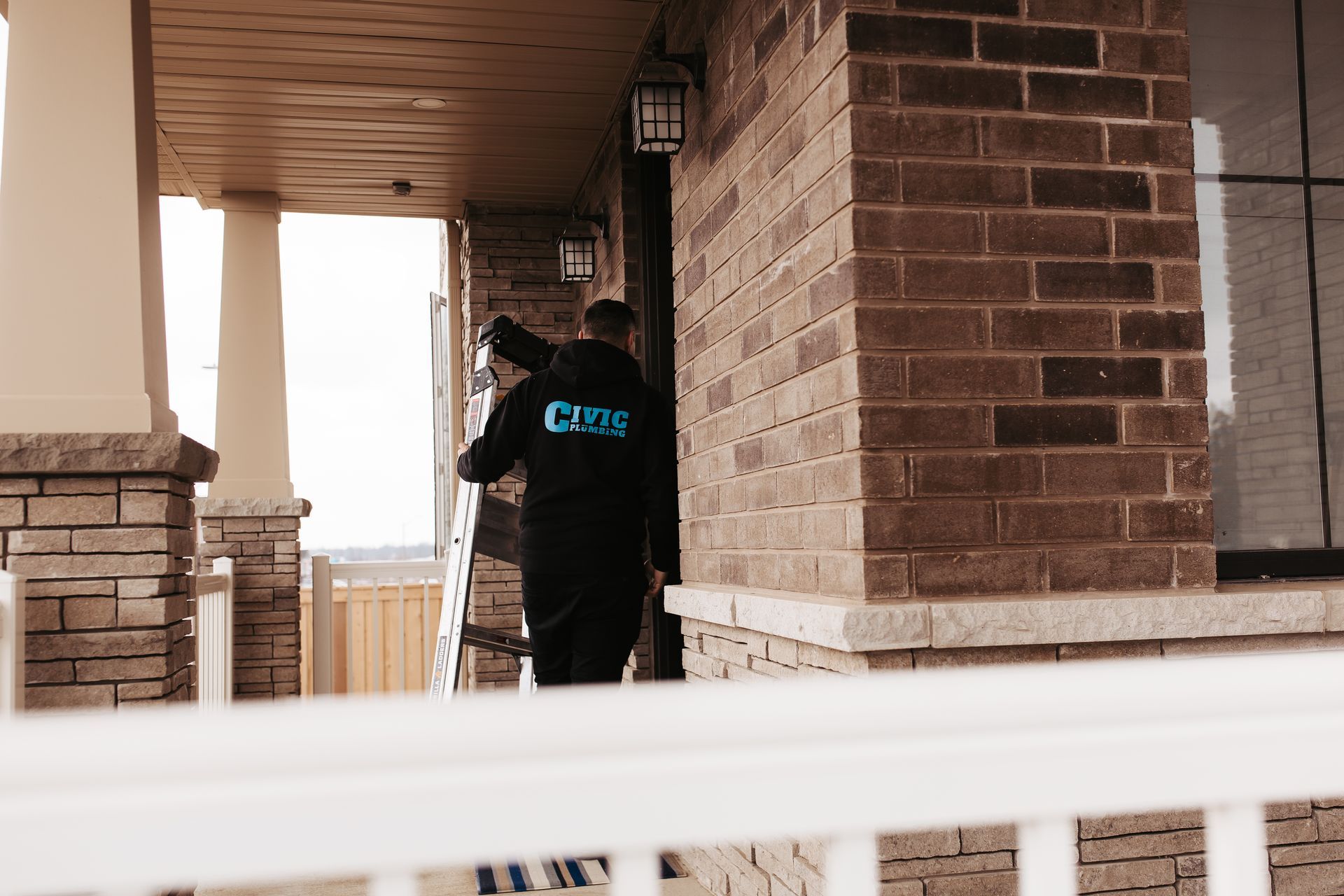 Person in a black jacket entering a brick building's entrance. The jacket has a blue logo. Porch columns are visible.