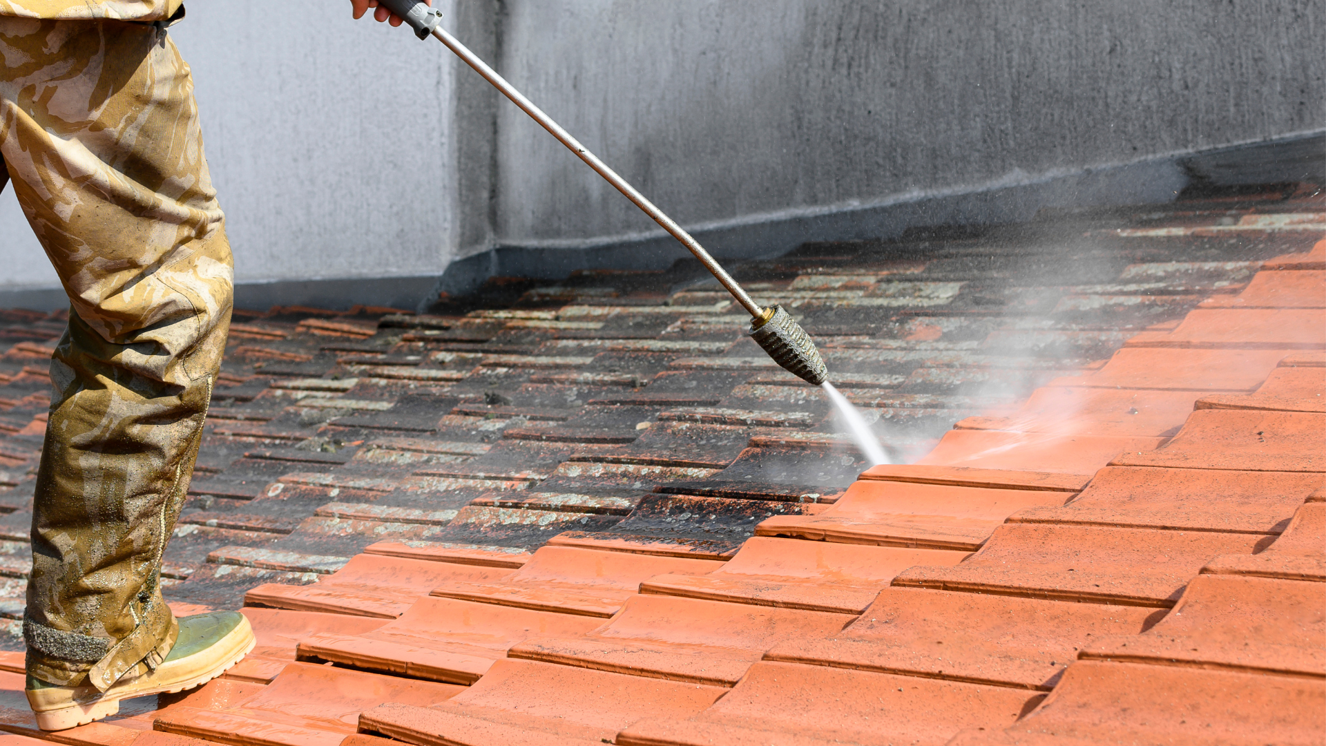Person power washing a red tiled roof, cleaning off dirt and debris.