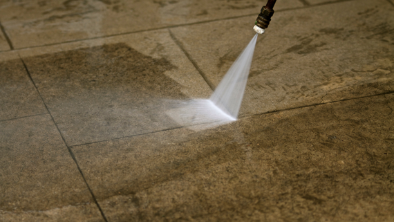 Pressure washer spraying water on stone tiles, cleaning them.