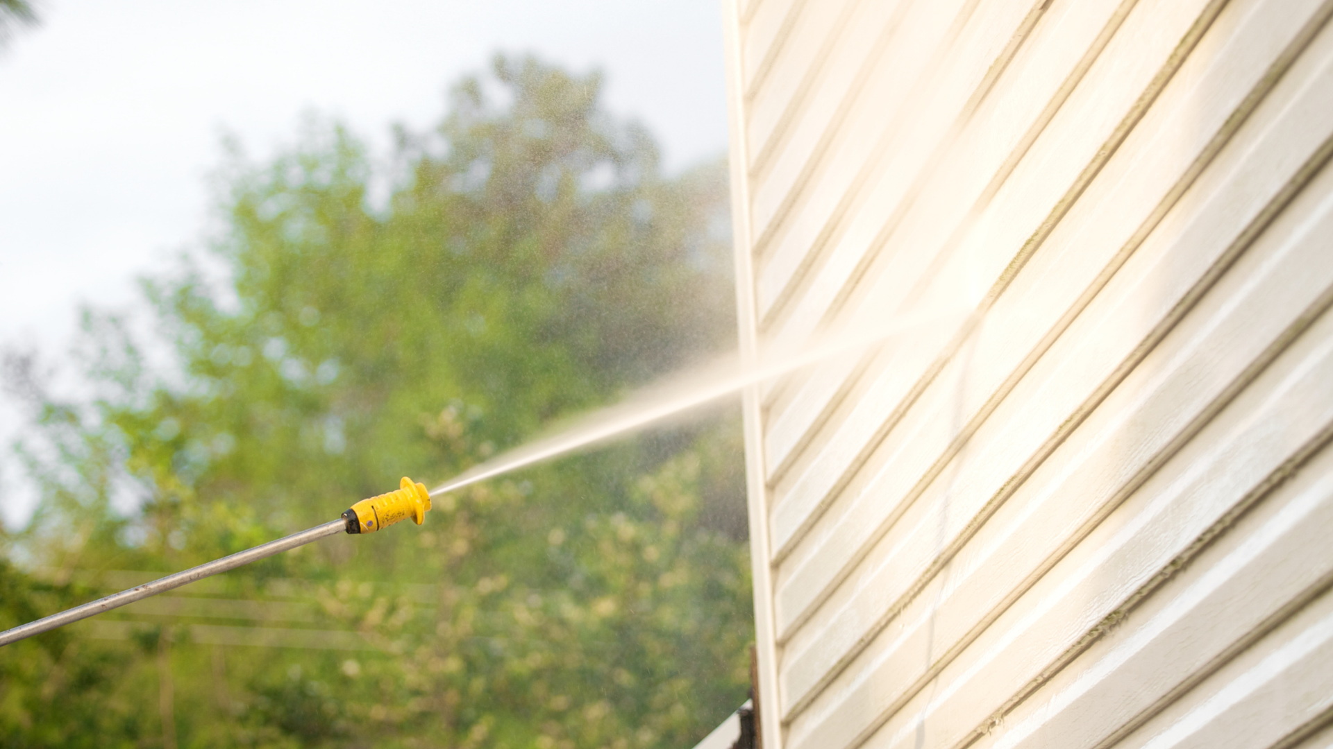 Power washer spraying a white siding on a house outdoors.