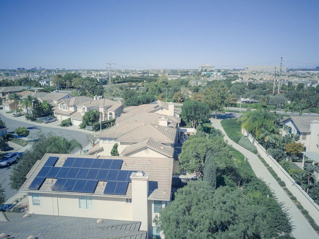 Aerial view of a house with solar panels on the roof in a suburban neighborhood under a clear blue sky.