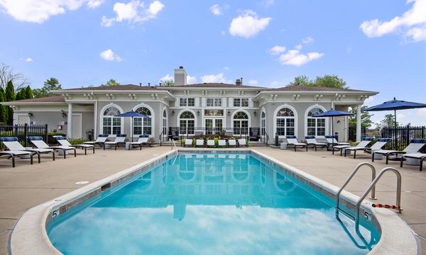 A large swimming pool surrounded by chairs and umbrellas in front of a large house.