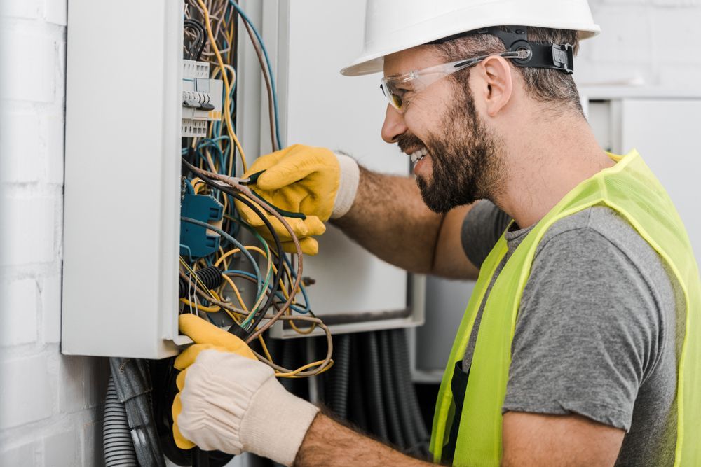 A man in a hard hat and safety vest is working on an electrical box.