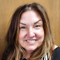 A woman with long hair is smiling in front of a wooden wall.
