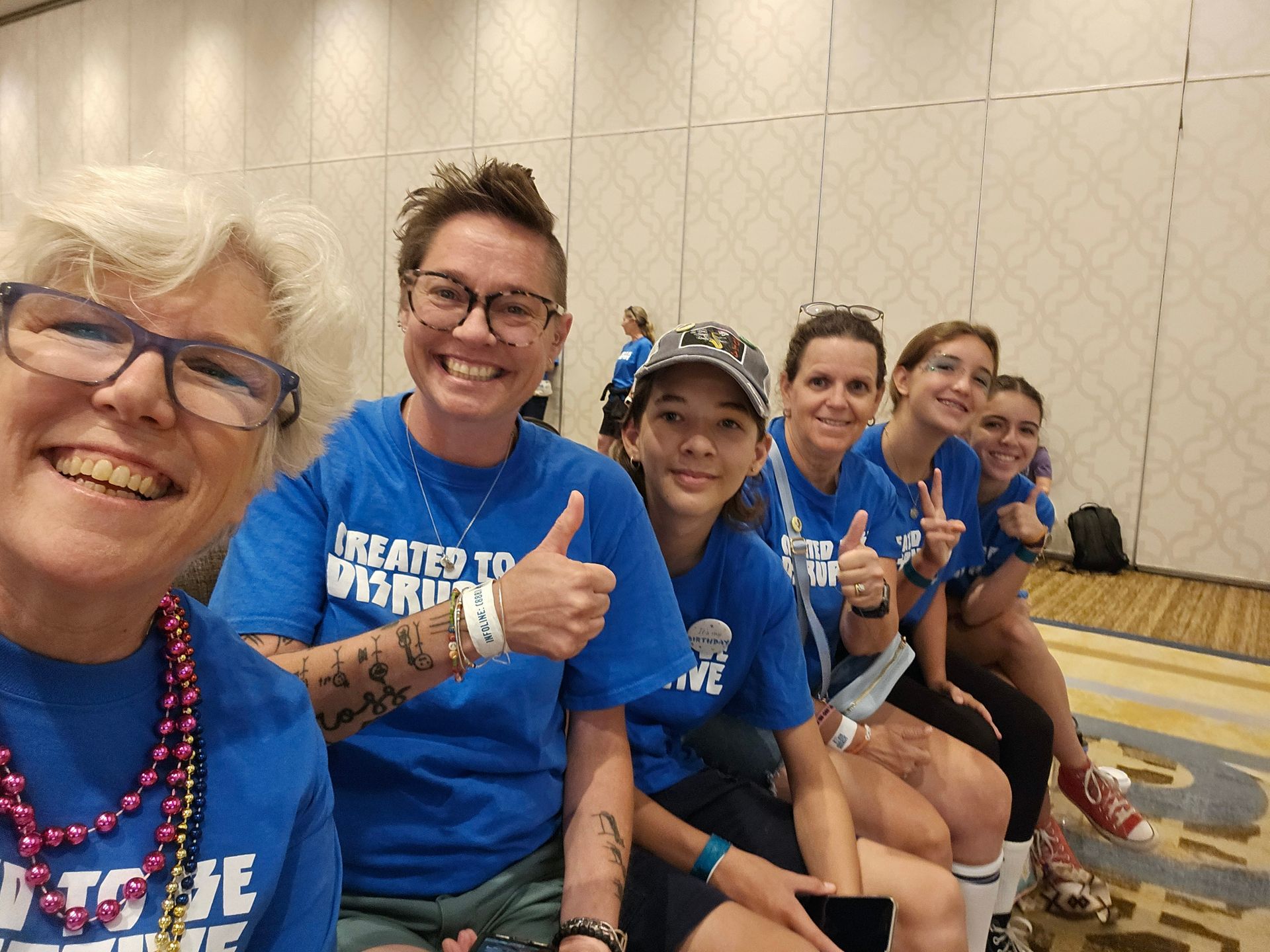 A group of women wearing blue shirts are sitting in a row and giving a thumbs up.