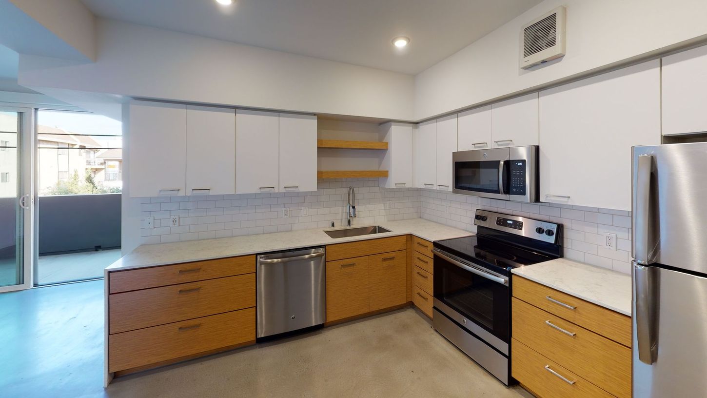 Modern kitchen with white and wood cabinets, stainless steel appliances, and a balcony.