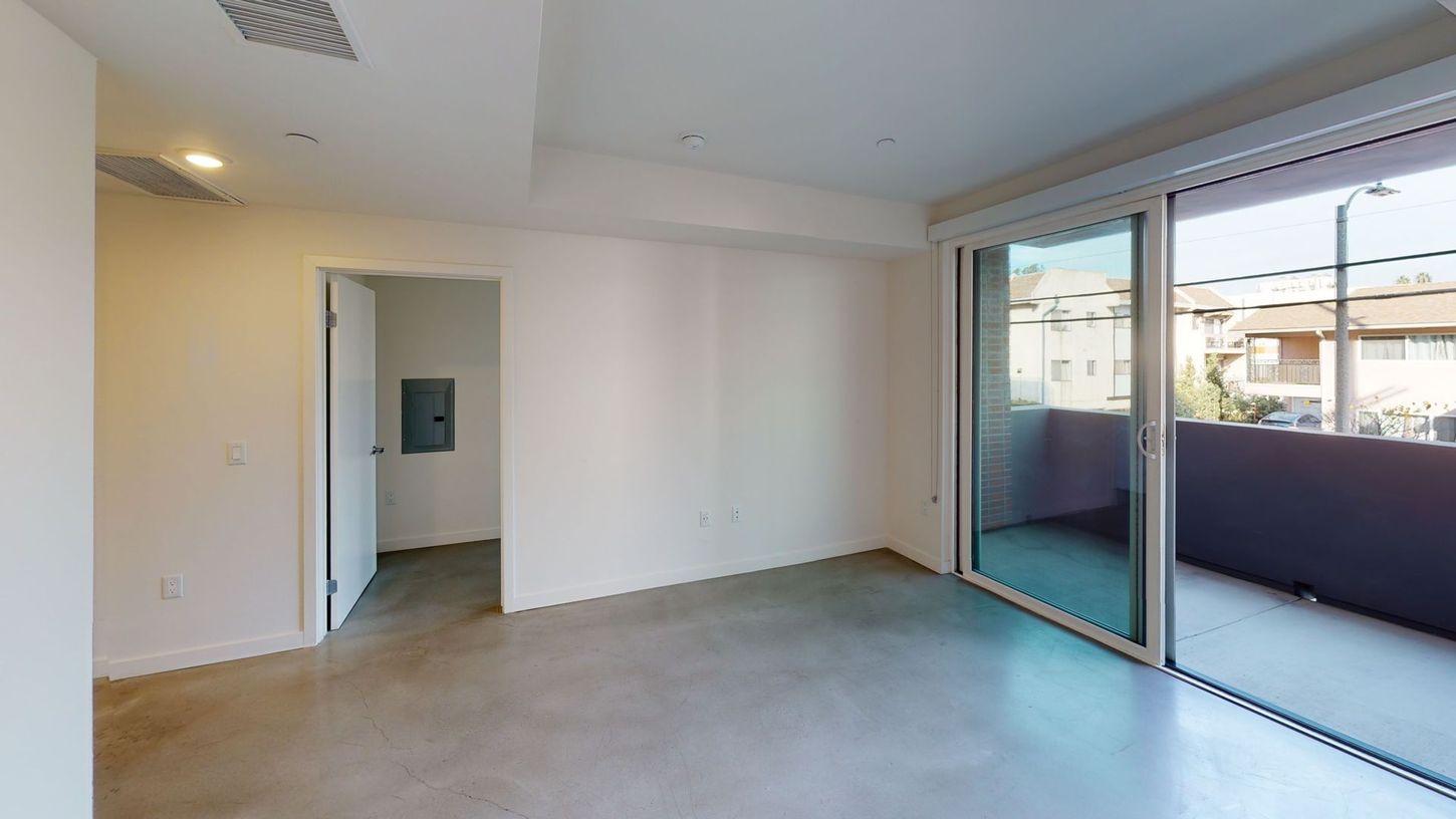 Empty modern living room with concrete floor, white walls, and sliding glass door to a balcony.