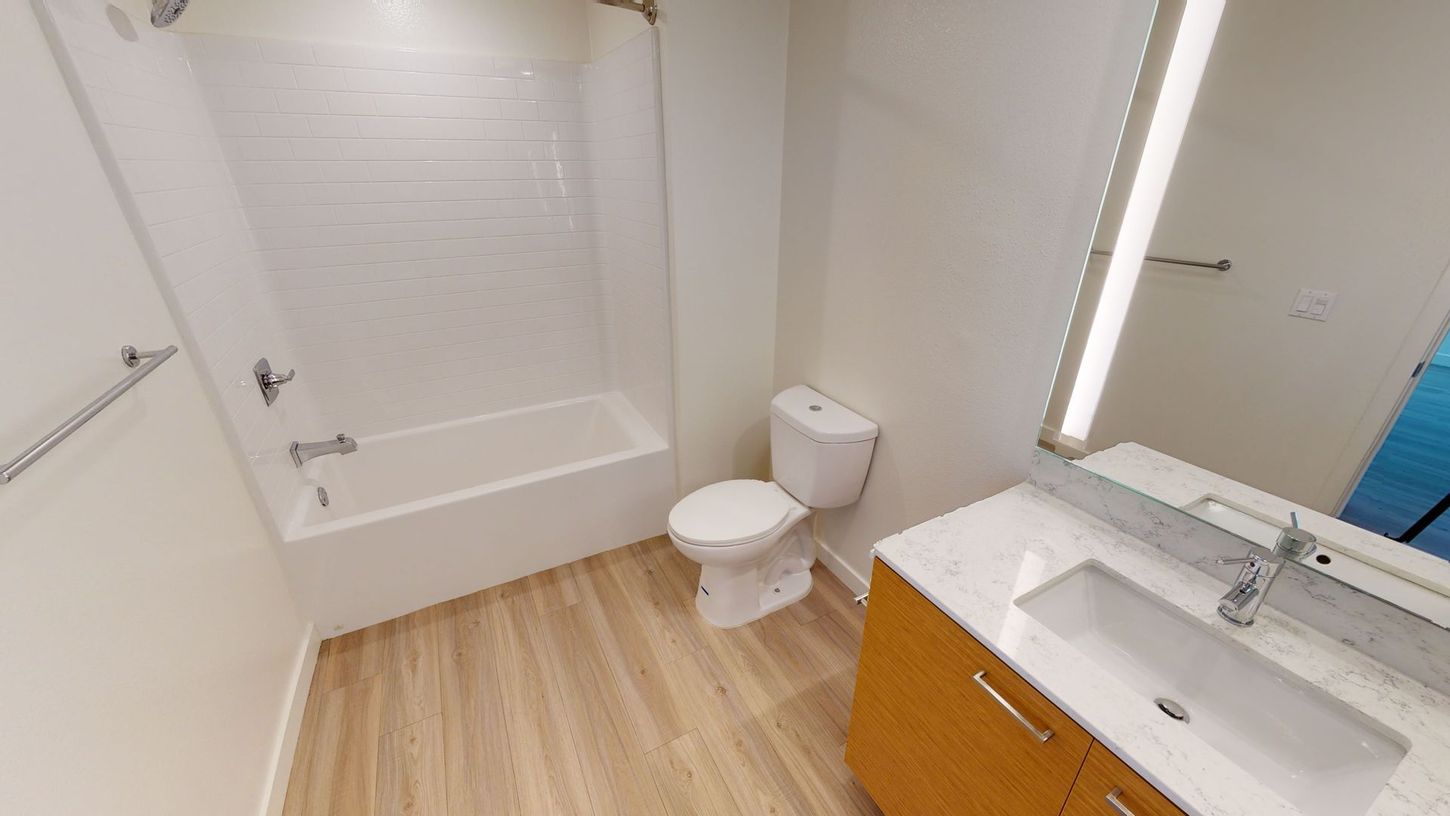 Bathroom with a white bathtub, toilet, and a wood vanity with a sink, light wood-look flooring.