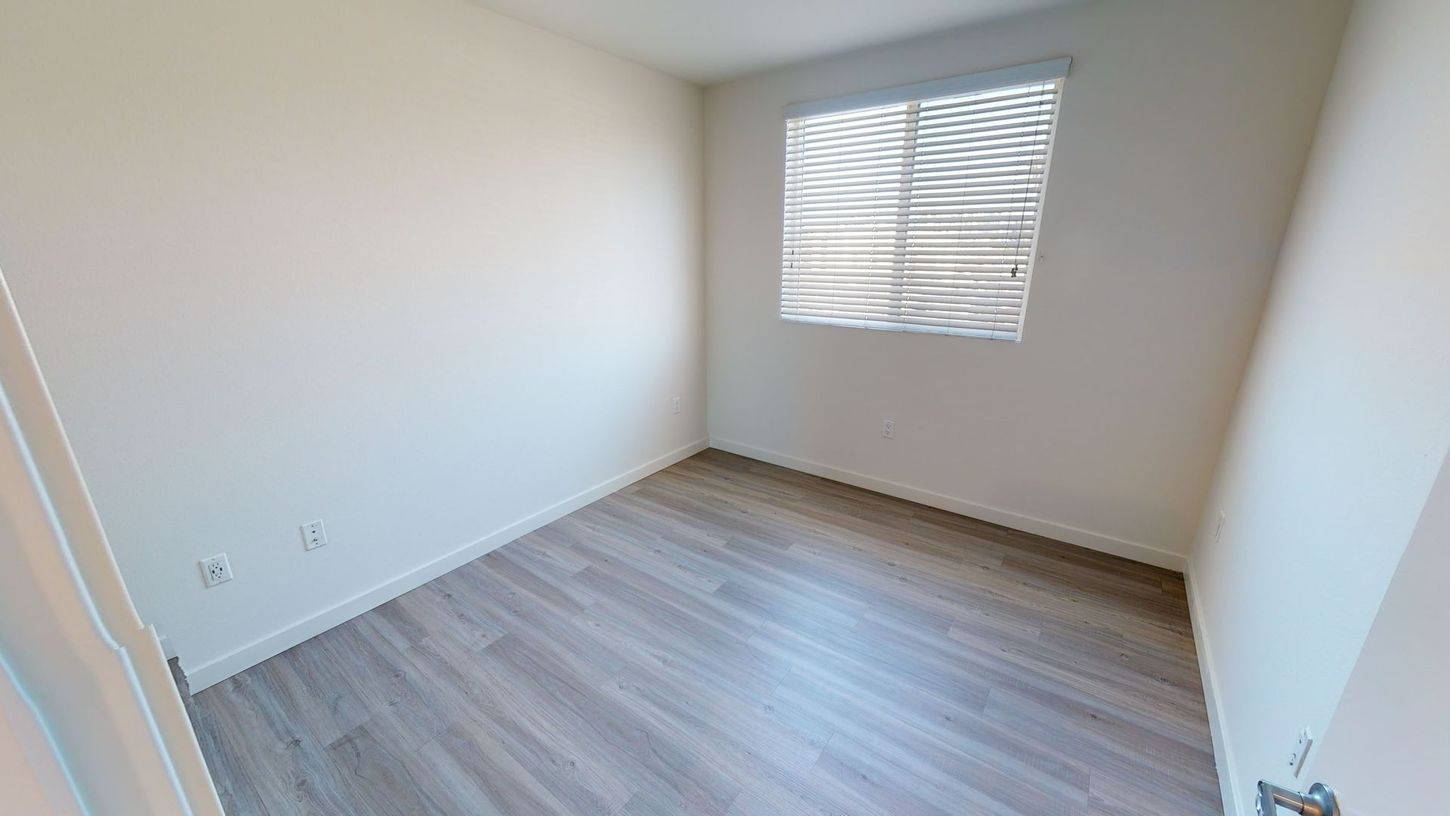Empty room with light gray flooring and white walls, window with blinds.