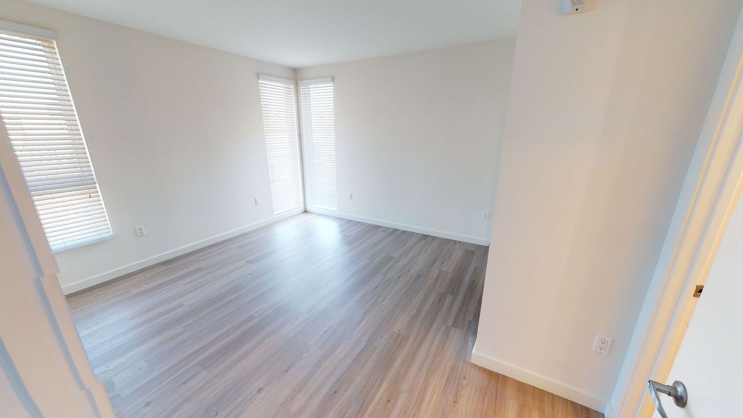 Empty room with light wood floor, white walls, and blinds.