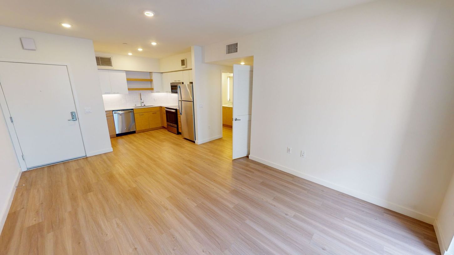 Empty apartment interior with kitchen, light wood floors, and white walls.