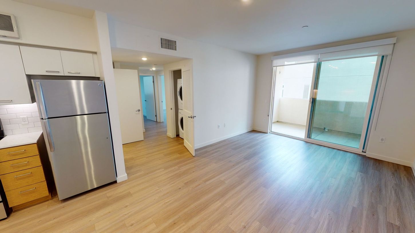 Apartment interior with fridge, cabinets, hallway, and sliding glass door to balcony.