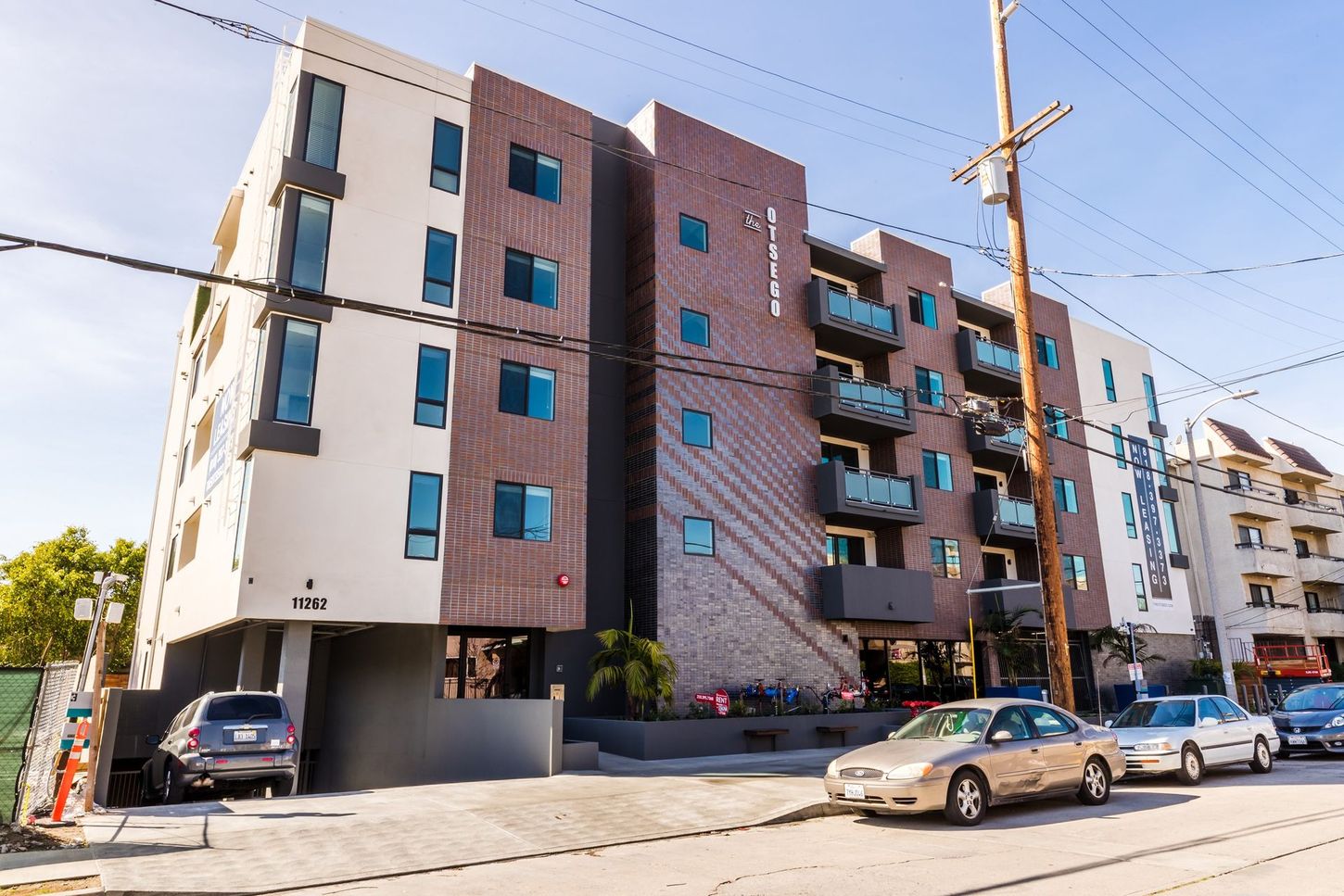Modern apartment building with a mix of light and dark brown facades. Cars parked on street.