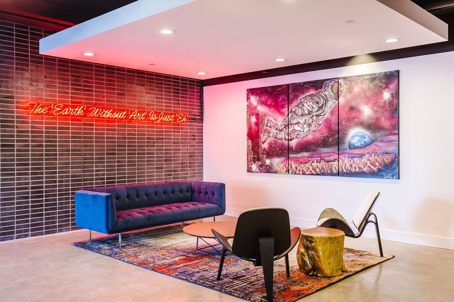Modern lounge with blue sofa, art, and neon sign reading 