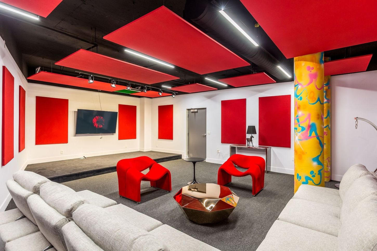 Red-accented entertainment room with soundproofing panels, a stage, seating, and a TV.