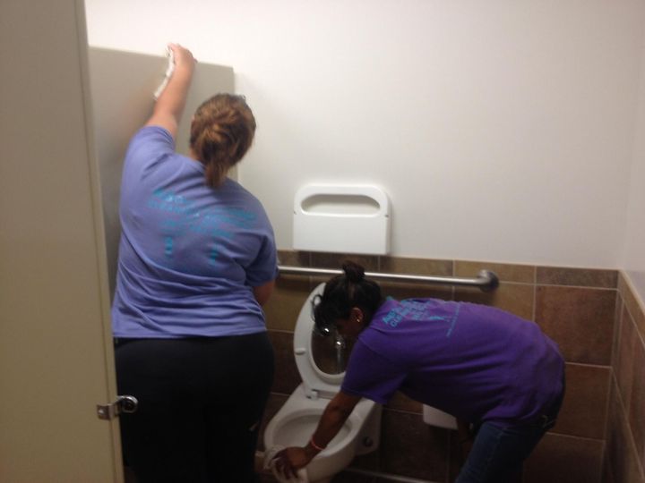 Two women are cleaning a toilet in a public restroom.