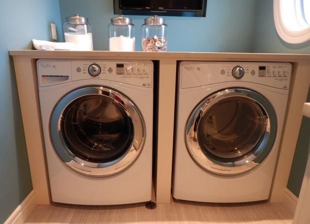 A washer and dryer are built into a wood cabinet with jars on top, in a room with blue walls.
