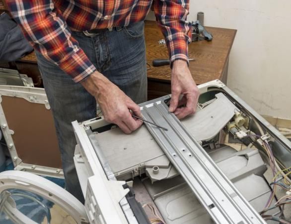Person repairing a disassembled washing machine, working with wires inside the open unit.