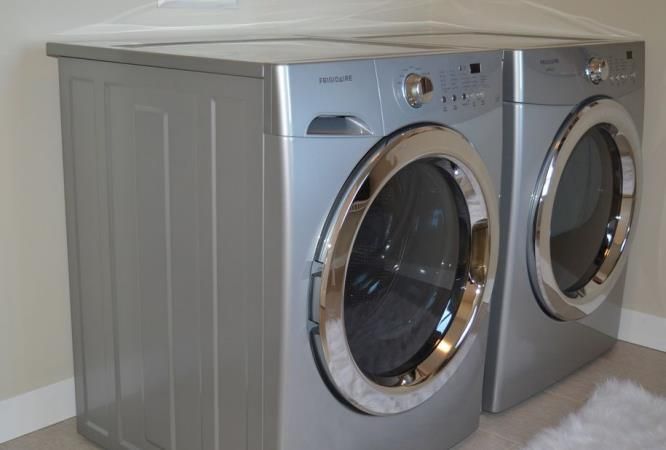 Silver washing machine and dryer set in a laundry room, with chrome detailing.