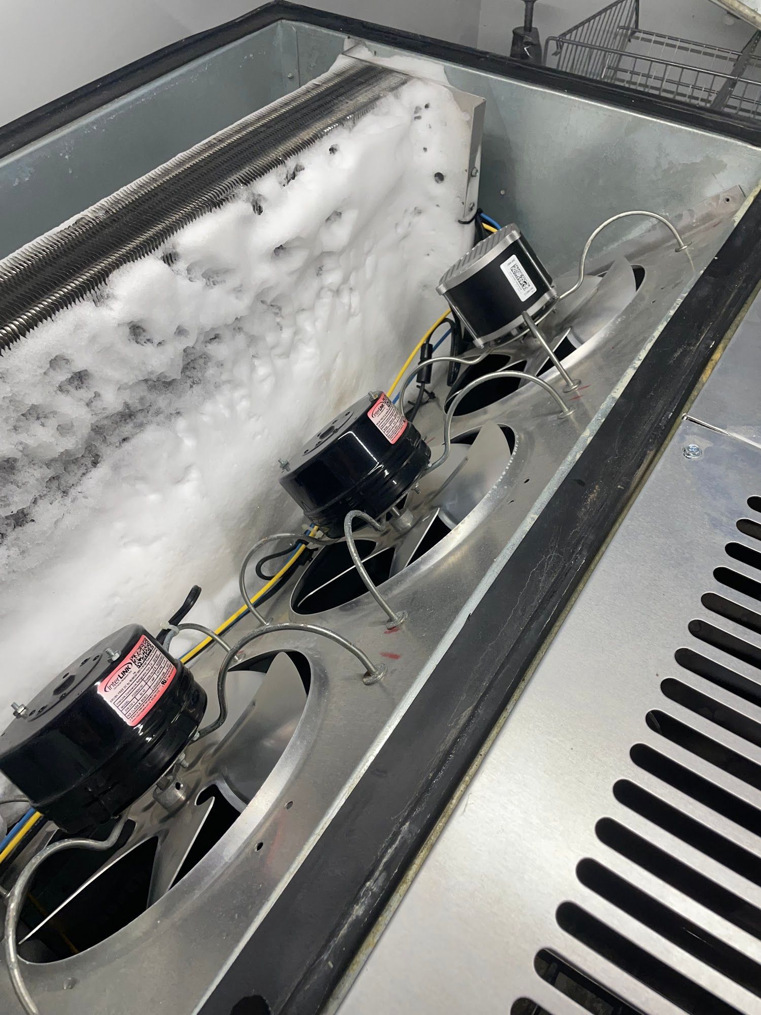 Interior of a freezer with heavy frost buildup and three fan motors visible.