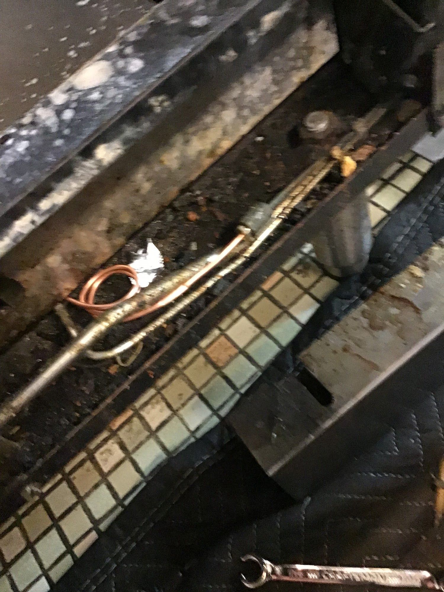 Close-up view of a dirty fireplace interior with a gas line, igniter, and burner components.