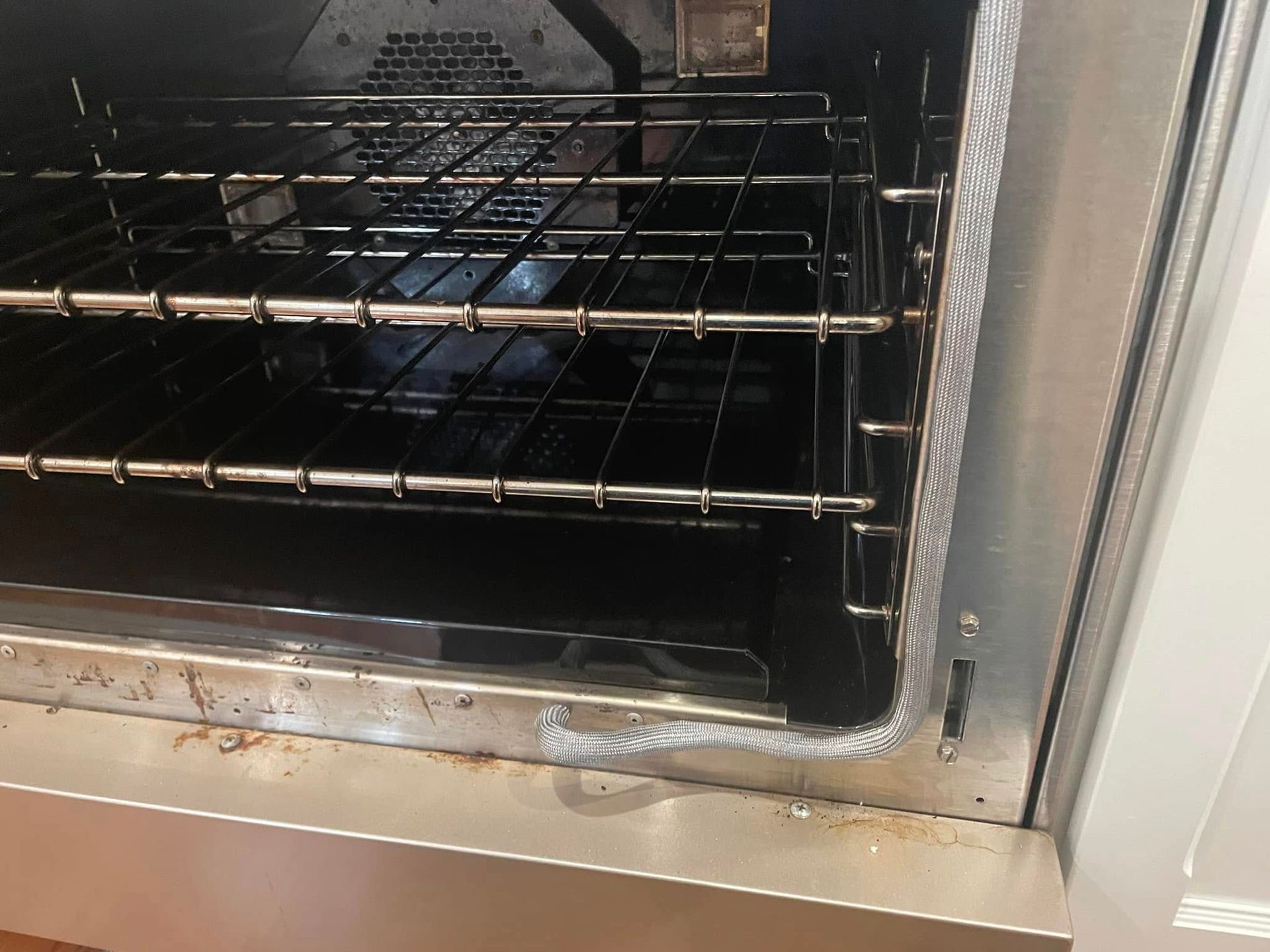 Inside of a dirty oven with multiple wire racks. The oven door is open with foil around the edge.