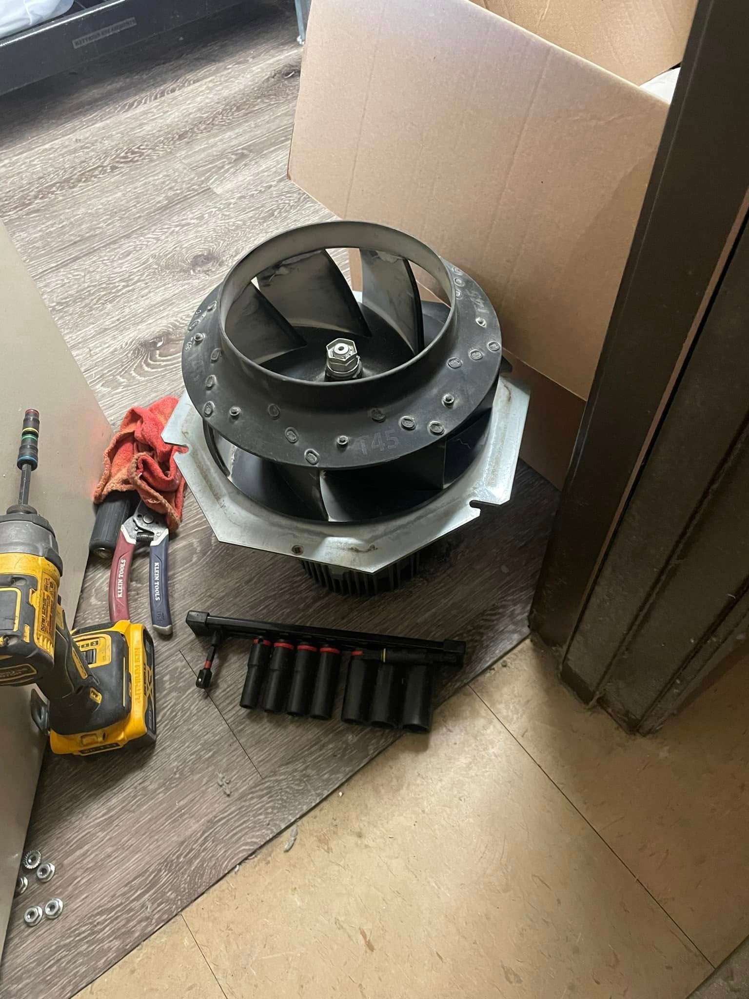 Furnace blower with tools on a rug. The blower is detached, with screws and a power drill nearby.