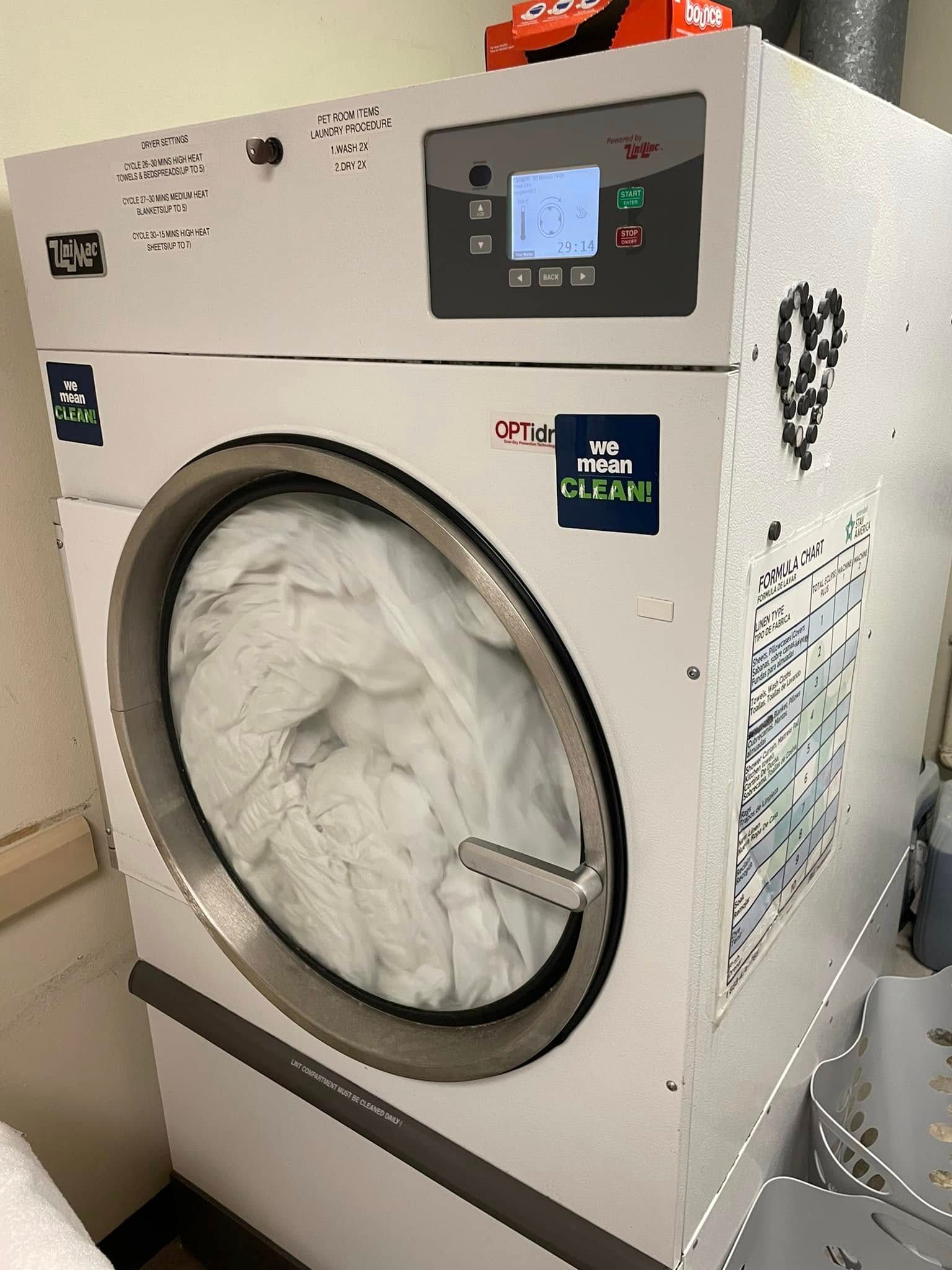 White commercial clothes dryer with laundry inside; control panel on top.