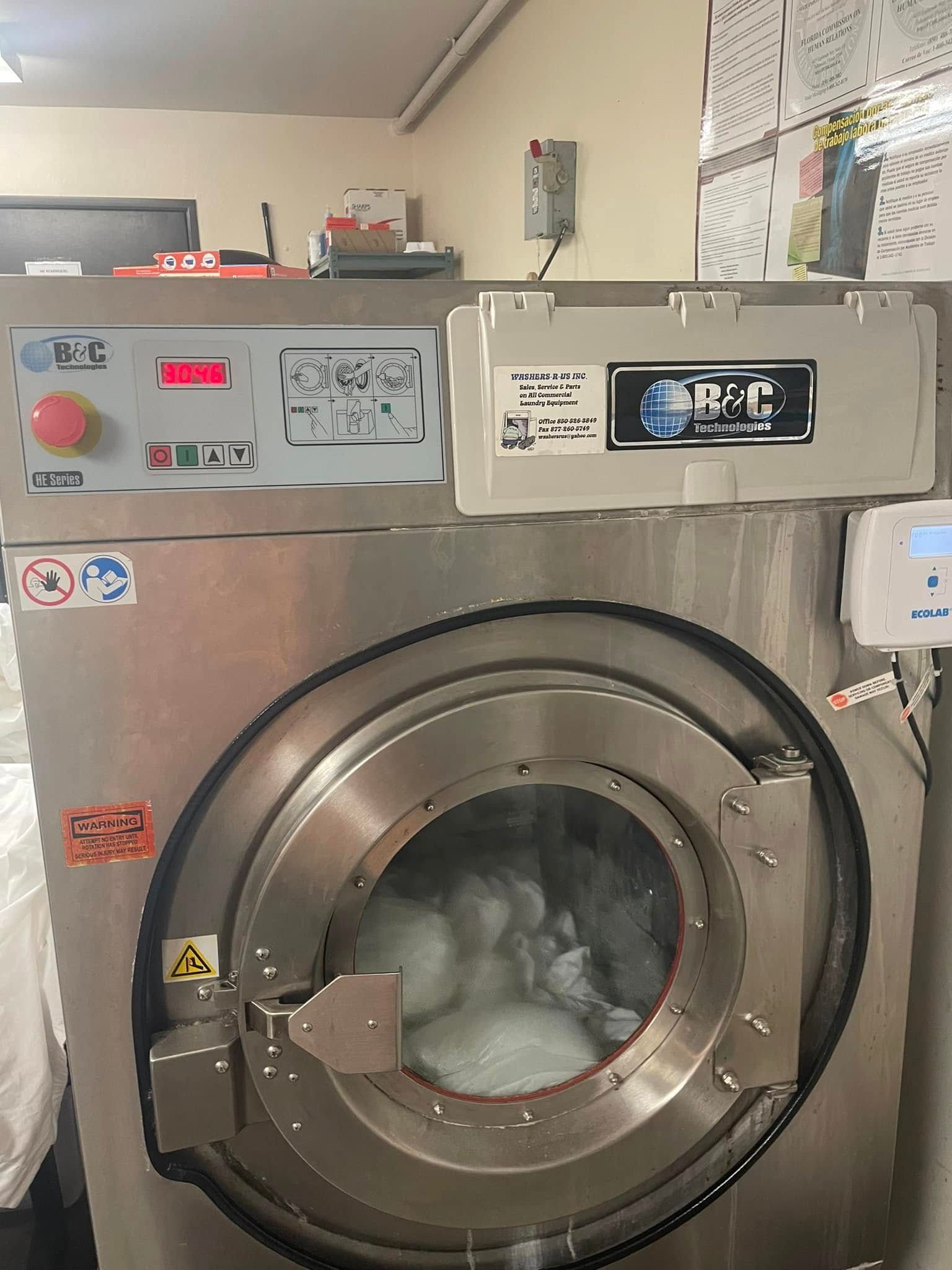 A commercial washing machine with a stainless steel drum, door closed, in operation, washing whites.