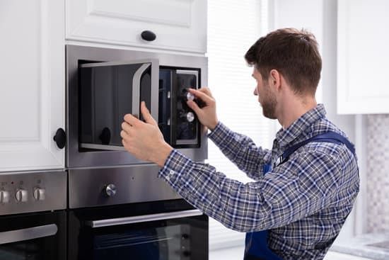 Man in plaid shirt opening built-in microwave door in a kitchen.