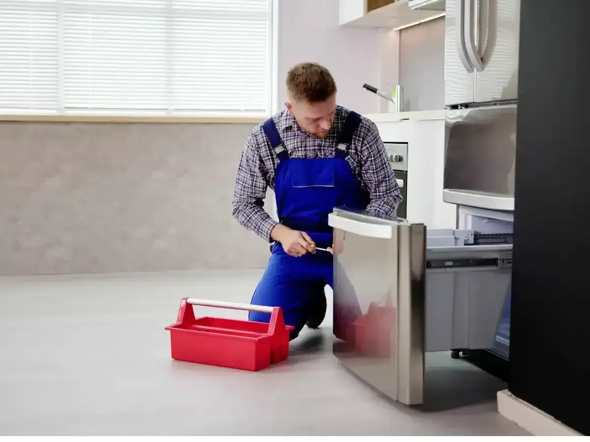 Technician kneels, writing on notepad next to a refrigeration unit, hoses, and a cylinder in a room.