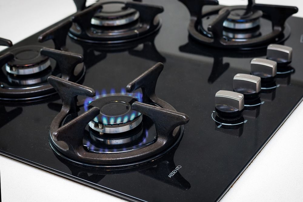 Black gas cooktop with four burners, three lit with blue flames, silver knobs.