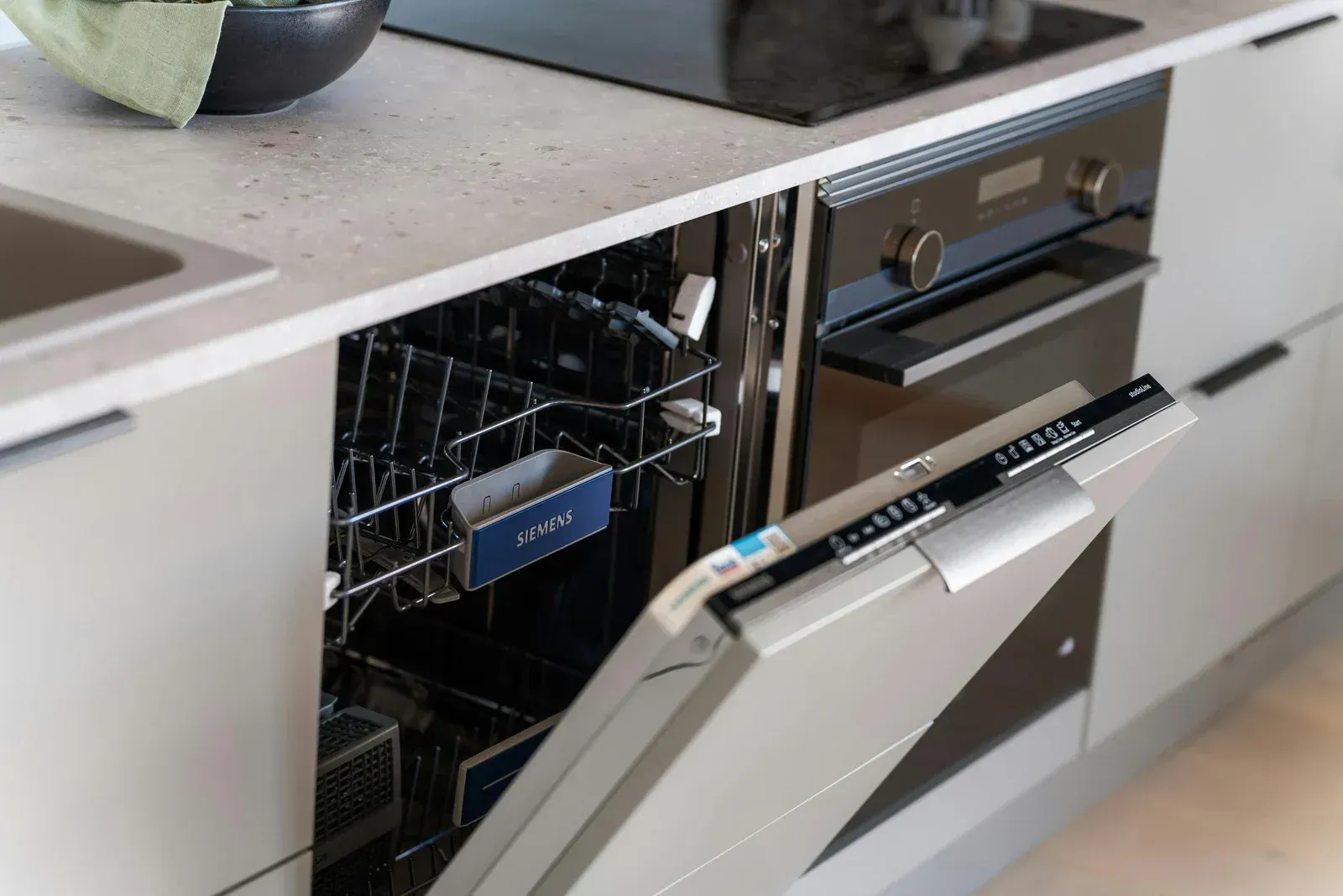 Dishwasher with open door, partially built-in, next to a black oven in a modern kitchen.