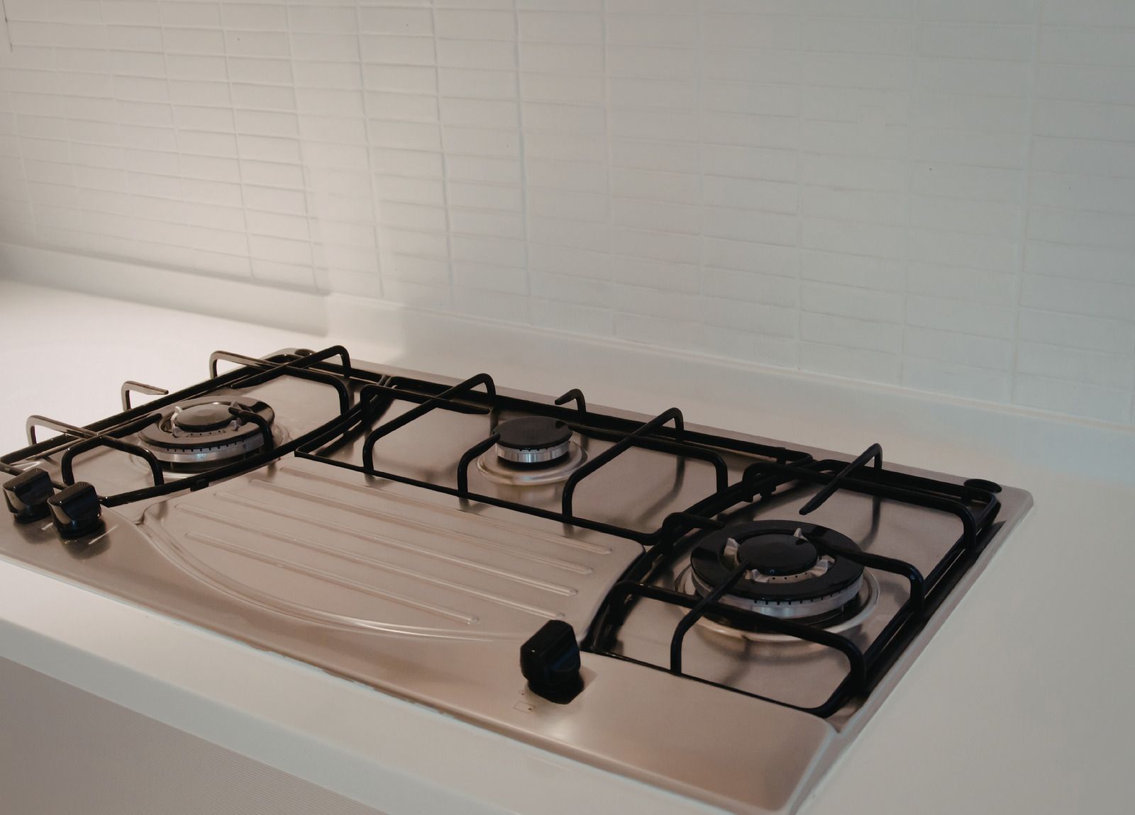 Stainless steel gas cooktop on white countertop with black grates and control knobs.