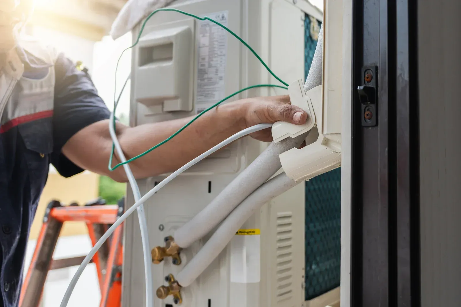 HVAC technician installing an air conditioning unit; wires and tubes visible.