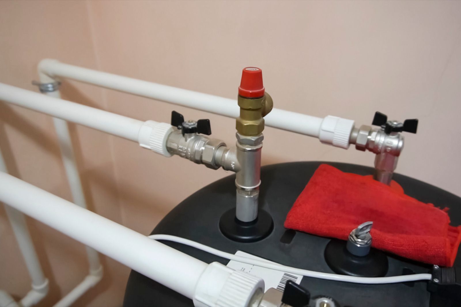 Pipes and valves connected to a black tank, a red safety valve, and white pipes, indoors.