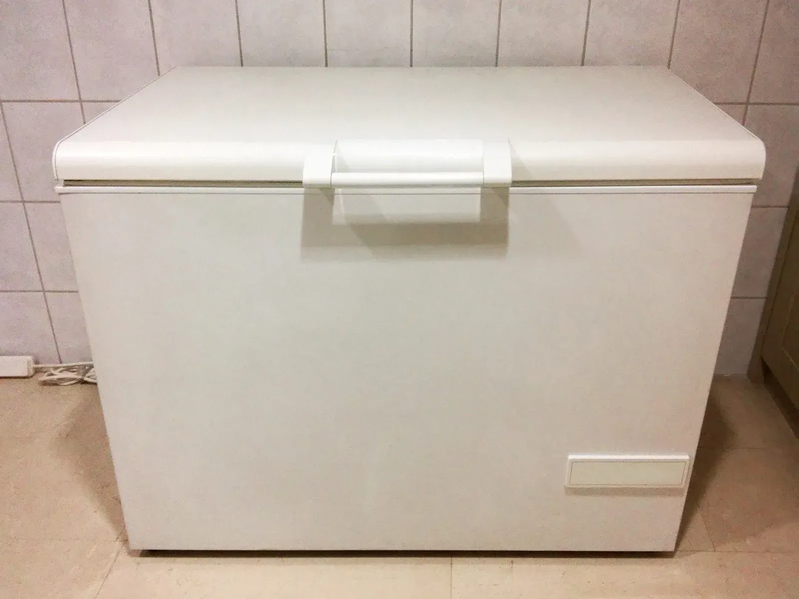 White chest freezer in a room with tiled walls and a beige floor.