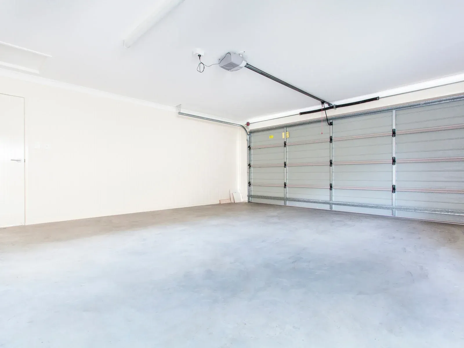 Empty, light-filled garage with a closed gray door, white walls, and a concrete floor.