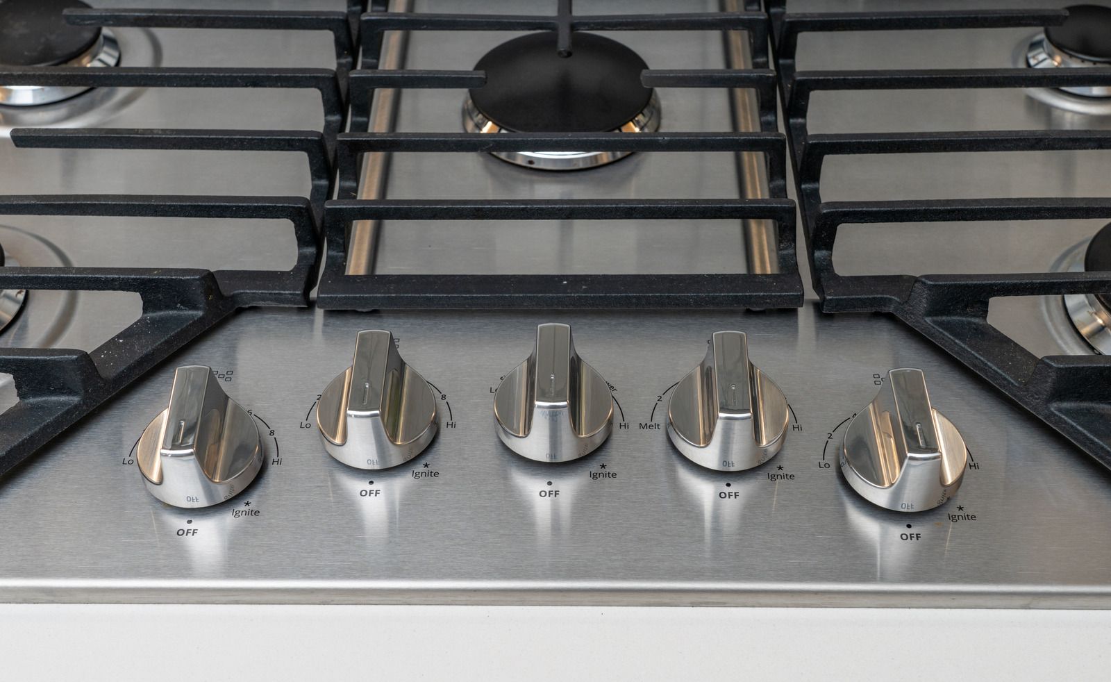 Close-up of a stainless steel gas stove with five silver knobs and black grates.